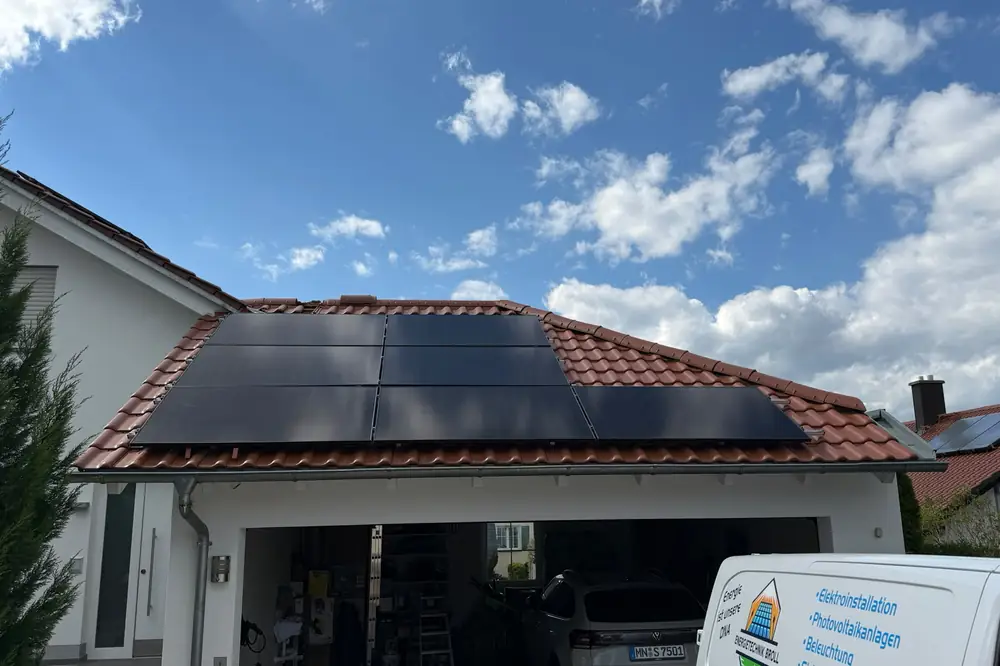 Photovoltaikanlage mit schwarzen Modulen auf einem Ziegeldach, davor ein Firmenwagen von Energietechnik Broll